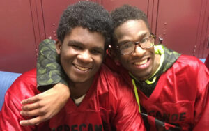 Tippecanoe County athlete Carlos Crawford with his arm around his friends neck, both wearing uniforms in the locker room.