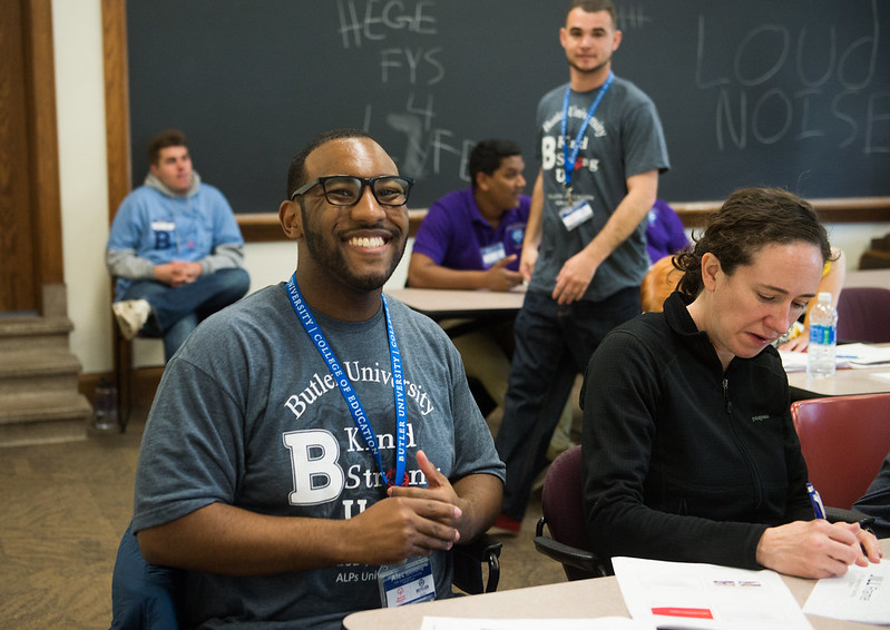 Two people at a table working. Man is smiling at the camera.