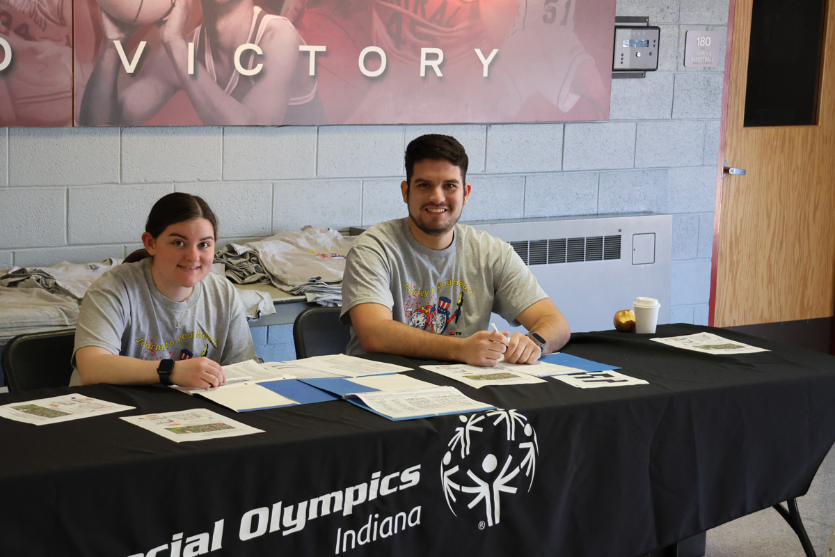 Man and Woman behind Special Olympics of Indiana desk with papers on it.