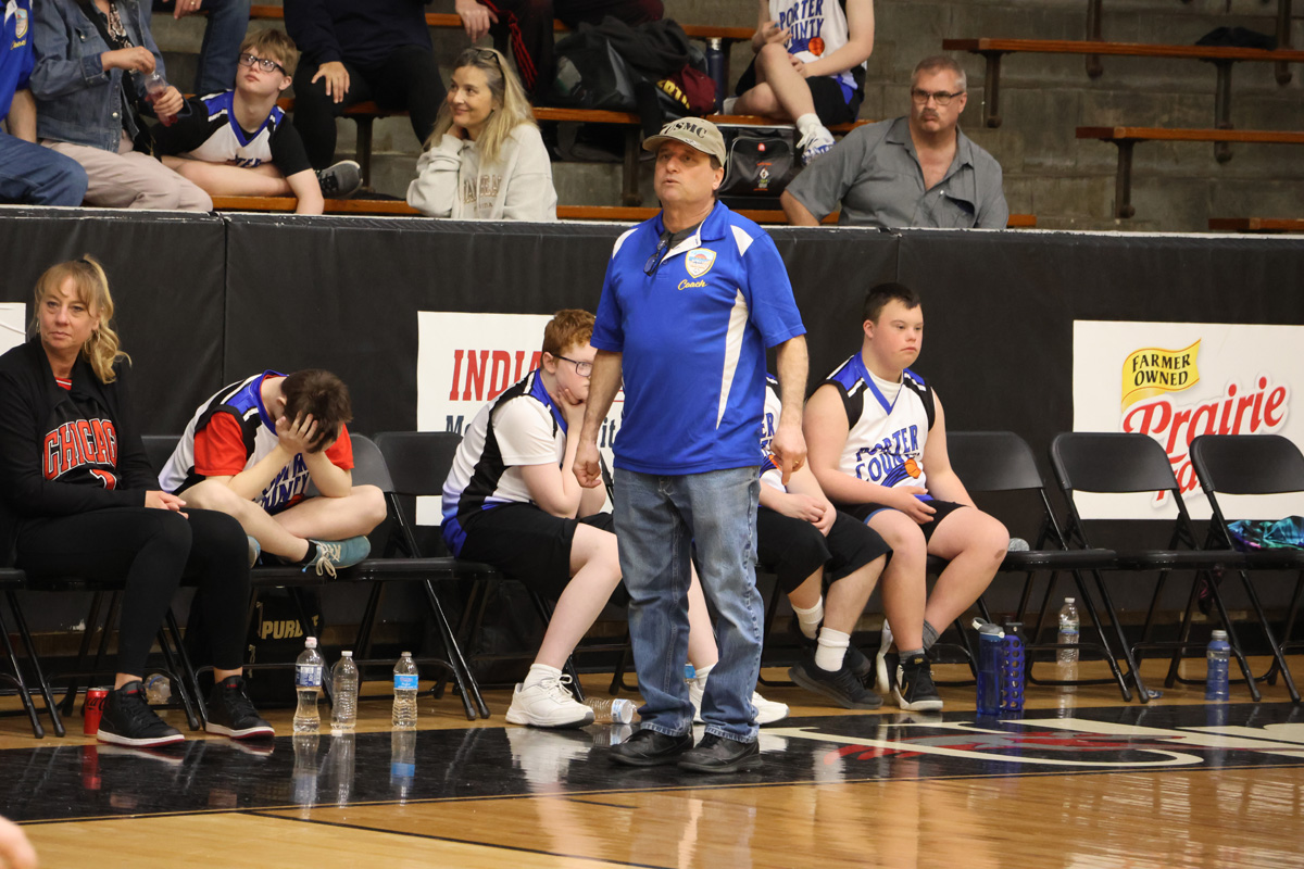 Coach standing on side lines watching game with blue shirt on.