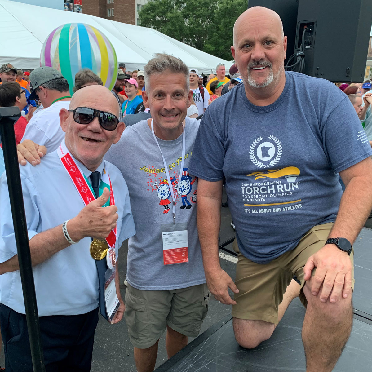 Three men smile for picture one with a thumbs up.