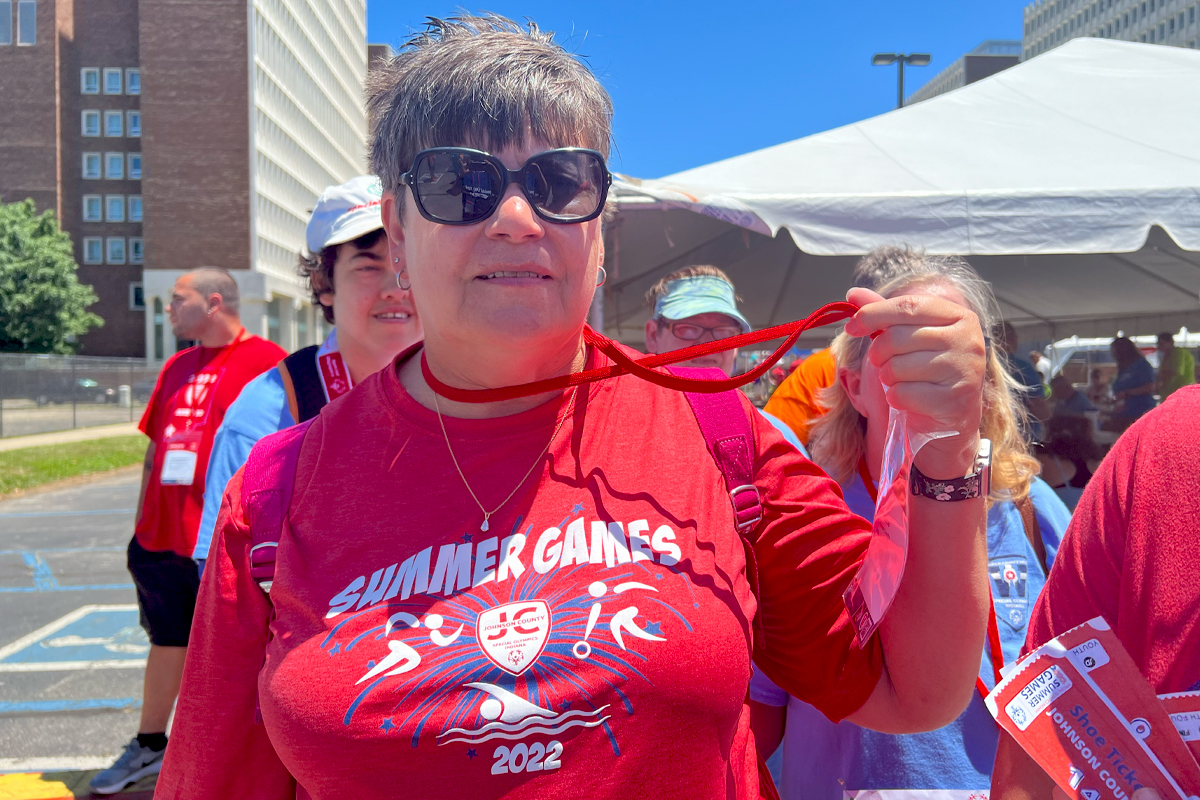 Woman in red shirt holding up a medal.